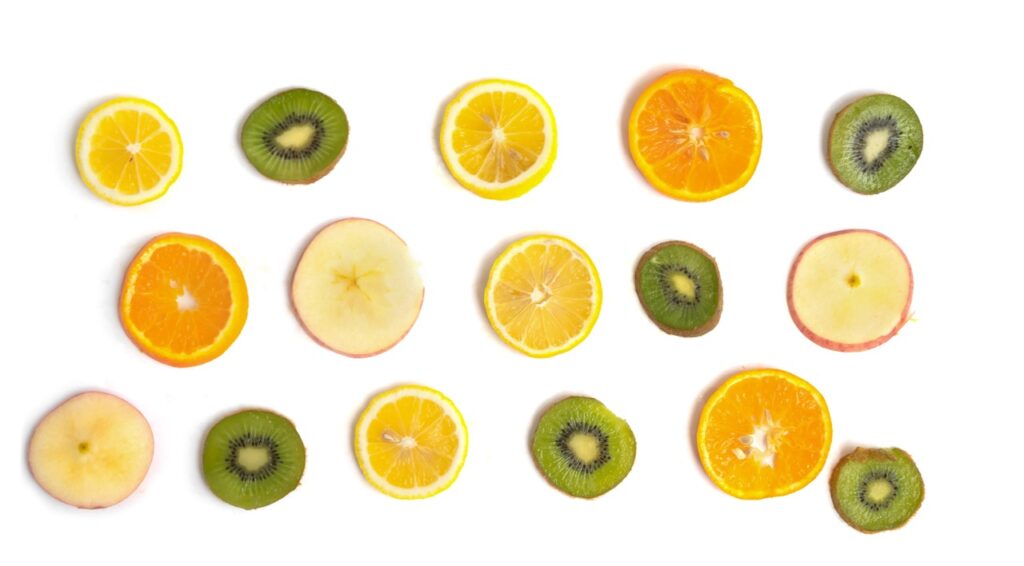 Pattern di fette sottili di frutta fresca mista con arancia, limone, kiwi e mela disposte su sfondo bianco.